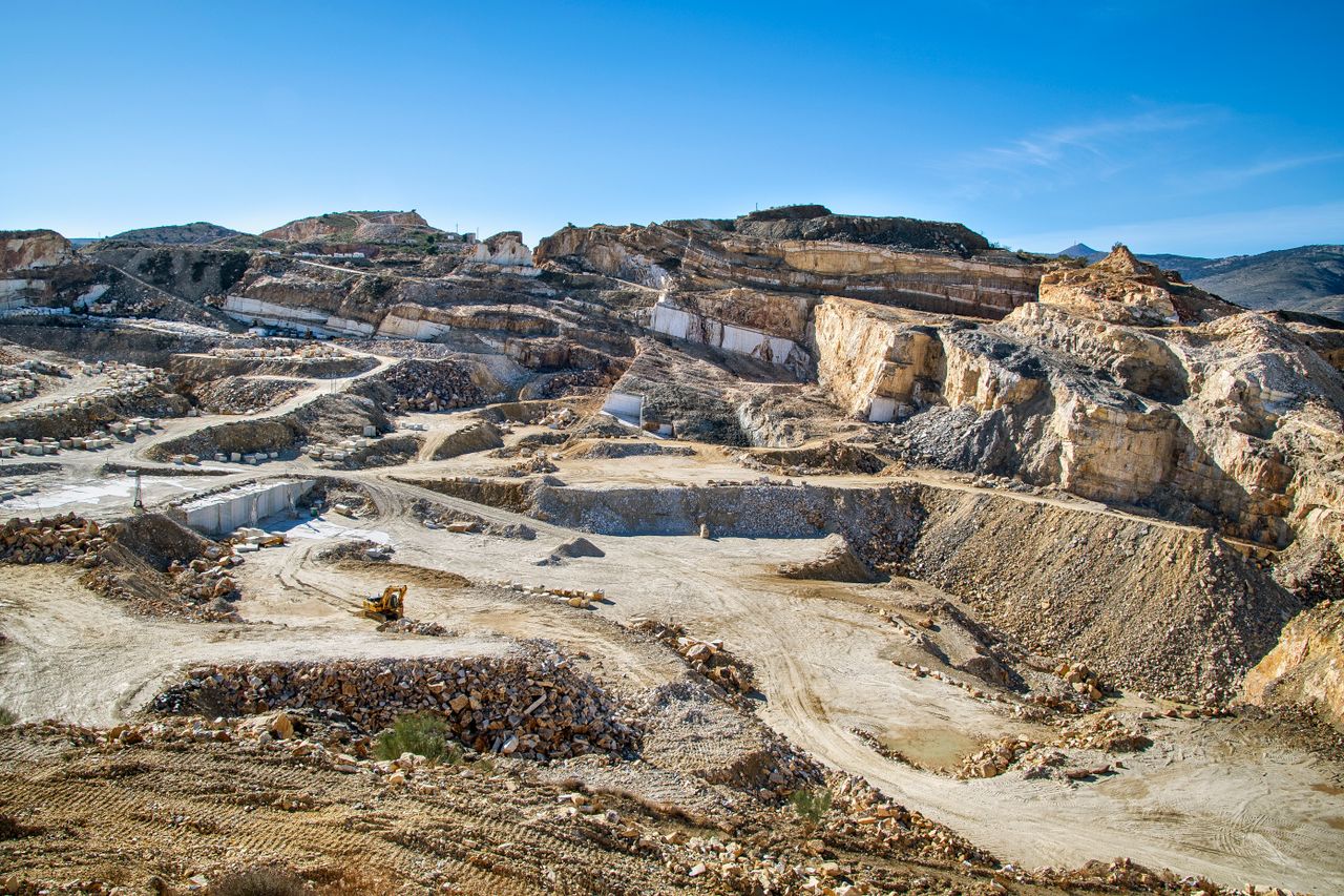Wide view of a large open-pit quarry showing layers of rock and active heavy machinery.