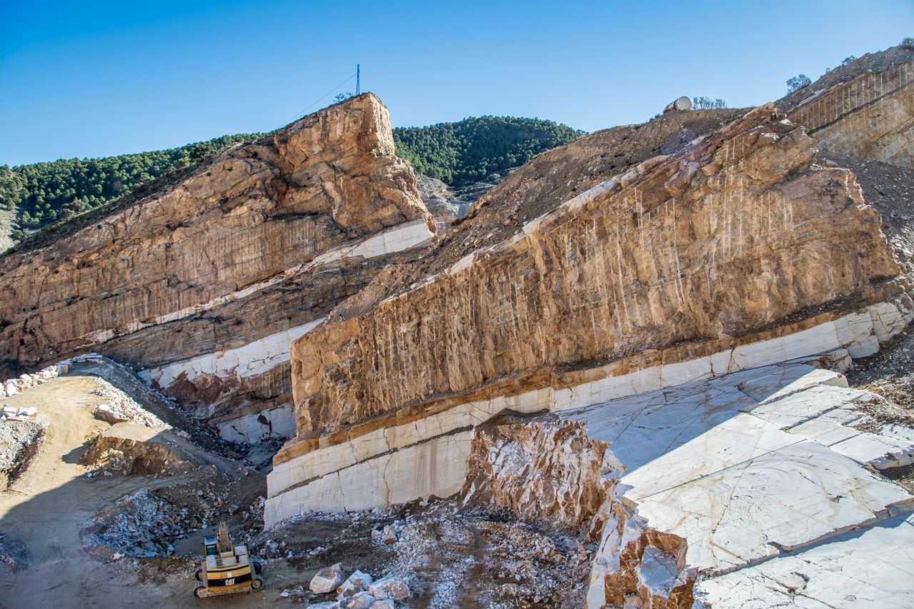 Aerial view of a vast rock quarry with an excavator amidst towering geological formations.